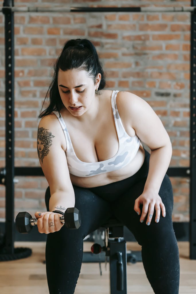 Serious plus size woman exercising with dumbbell in sports club